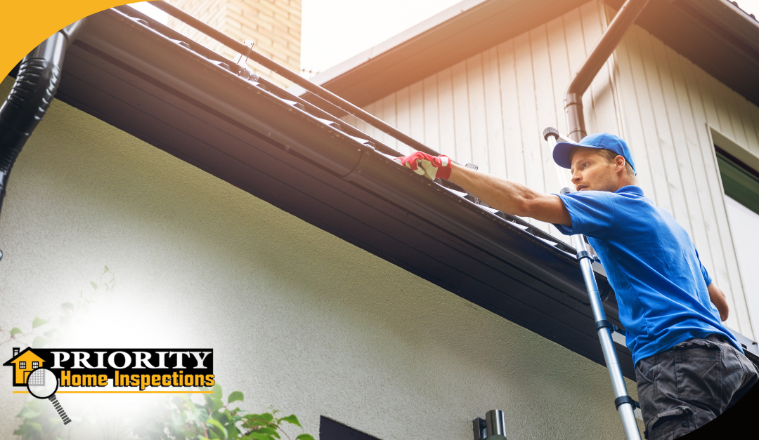 A professional home inspector wearing a blue uniform and cap is seen inspecting the gutters of a two-story home.